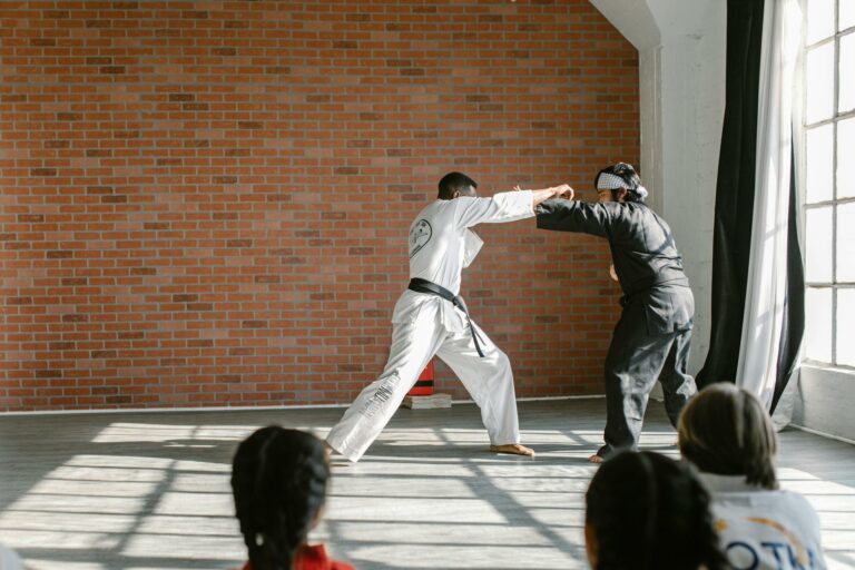 Martial artists practicing techniques indoors with sunlit brick background.