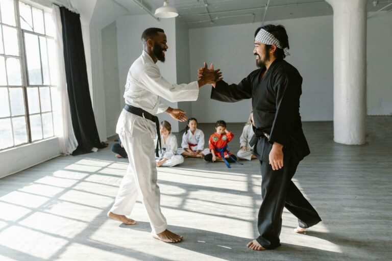 Two martial arts instructors demonstrating a handshake of respect in a sunlit dojo while students observe.